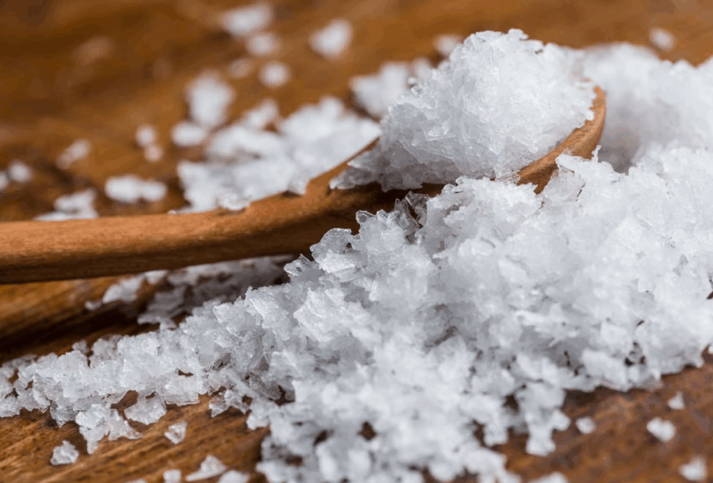 나무 테이블 위에 올려진 플레이크형 천일염, 바삭하고 얇은 결정 구조가 돋보이는 고급 소금